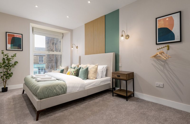 Modern bedroom with double bed, green and gold accents, wooden headboard feature wall, and framed artwork