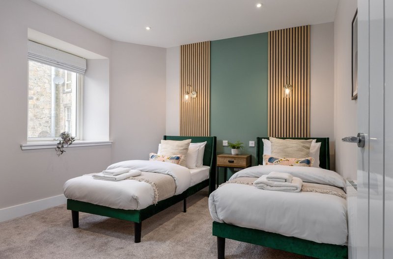 Twin bedroom with two single beds, green headboards, wooden slat feature wall, window and pendant lighting