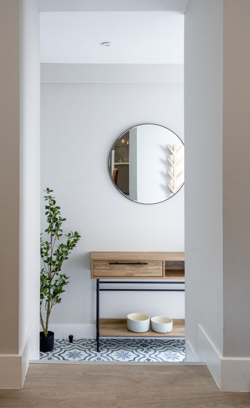 Modern entryway with round mirror, wooden vanity, potted plant and decorative rug