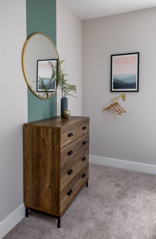 Hallway with wooden dresser, round mirror, framed landscape artwork and green accent wall