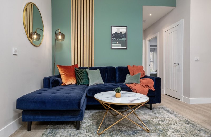 Modern living room with navy blue sectional sofa, colorful cushions, round marble table, and teal accent wall