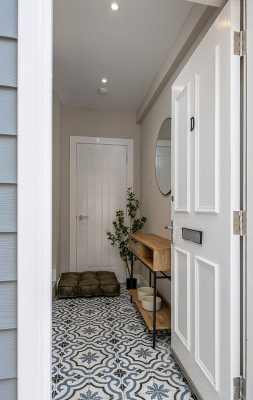 Modern entryway with patterned tile floor, wooden bench, mirror, and white doors