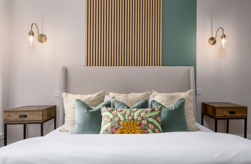 Modern bedroom with gray upholstered headboard, white bedding, decorative pillows, and brass pendant lights