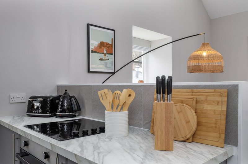 Modern kitchen with marble countertop, black appliances, wooden utensils and woven pendant lamp