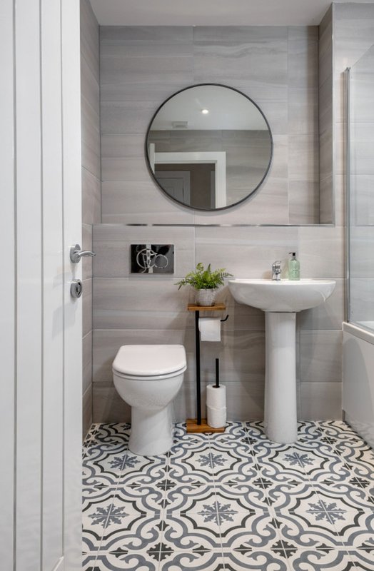 Modern bathroom with pedestal sink, toilet, round mirror, and patterned floor tiles