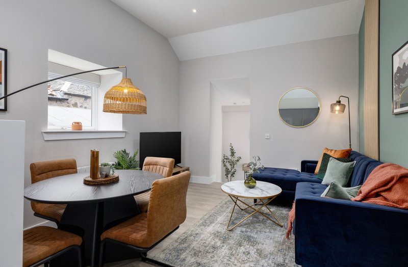 Modern open-plan living area with dining table, blue sofa, pendant lighting and decorative accessories
