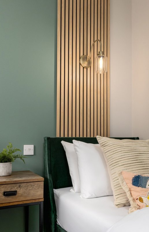 Modern bedroom with green upholstered bed, wooden headboard panel, white pillows, and pendant lighting