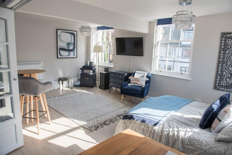 Bright studio apartment with bed, sofa, dining area and mounted TV near windows