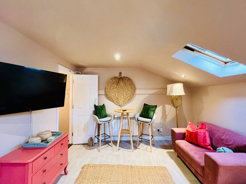 Bright attic room with TV, pink dresser, burgundy sofa, bar seating and skylight