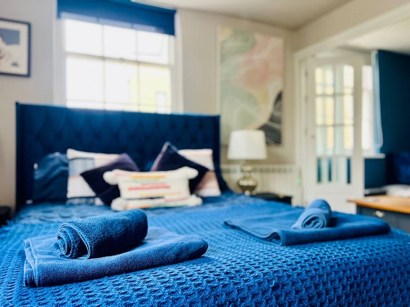 Bright bedroom with blue upholstered headboard, rolled towels on bed, and nautical décor