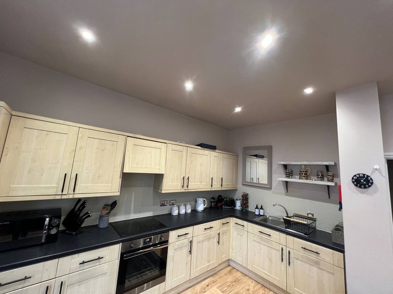 Modern kitchen with cream cabinets, black countertops, integrated appliances and recessed lighting