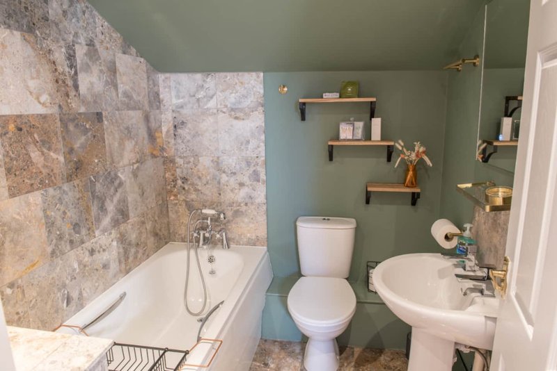 Bathroom with bathtub, toilet, sink, shelving and natural stone tile surround
