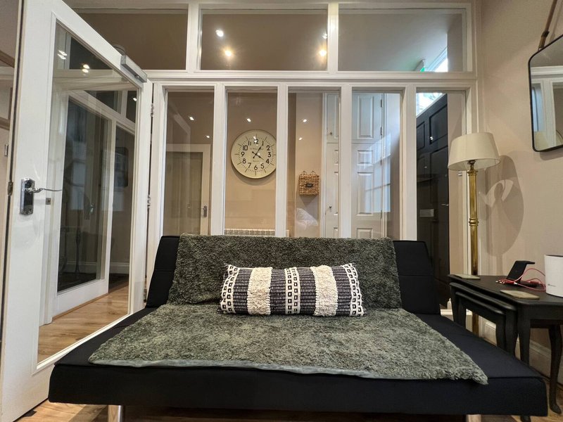 Modern bedroom with black bed, patterned bedding, white French doors, wooden flooring and wall clock