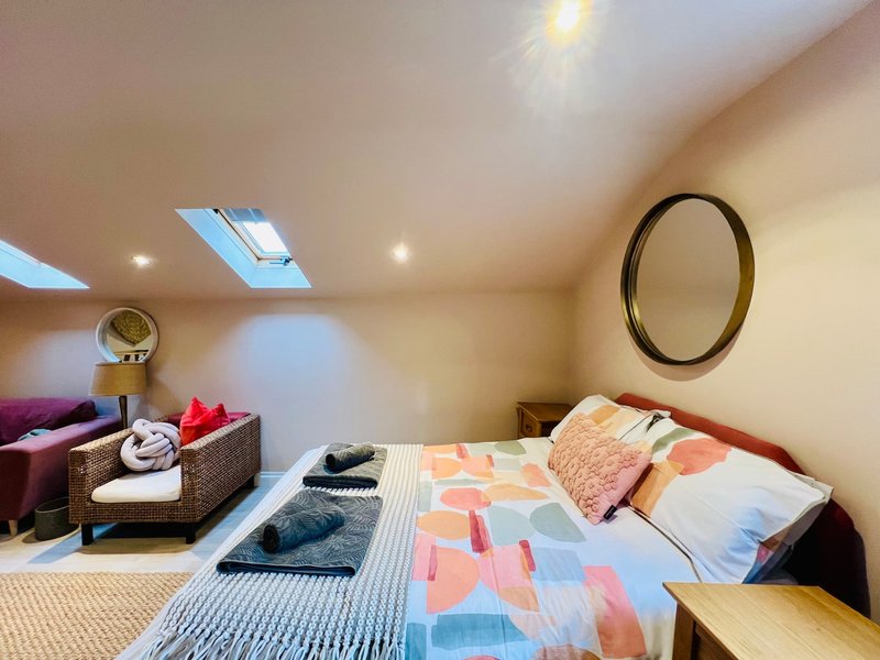 Attic bedroom with skylight, double bed, patterned bedding, wall mirror and storage furniture