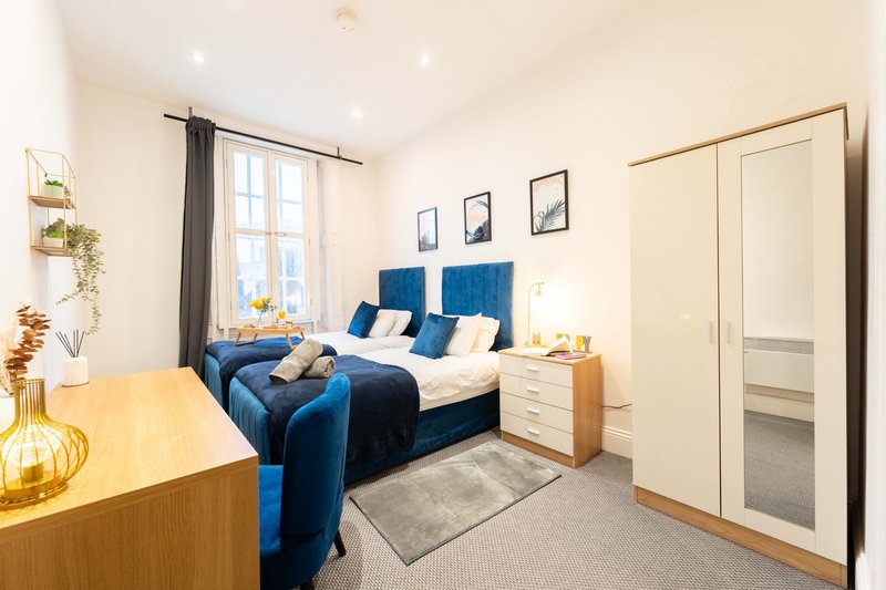 Modern bedroom with blue upholstered bed, wooden furniture, and neutral décor throughout