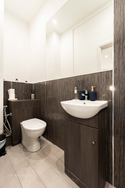 Modern bathroom with dark wood vanity, white sink, toilet, and bright lighting