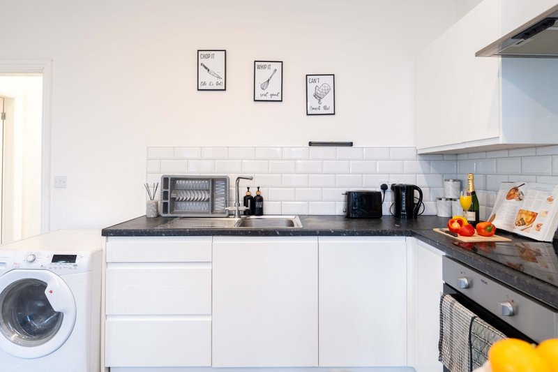 Modern kitchen with white cabinetry, black countertop, subway tile backsplash, and integrated appliances