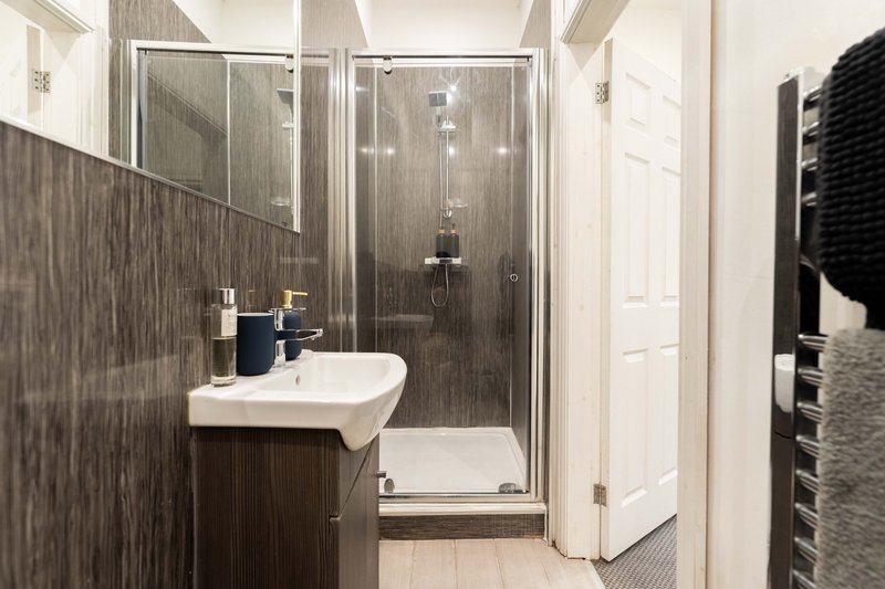 Modern bathroom with dark tile walls, white sink, glass shower enclosure and towel rail