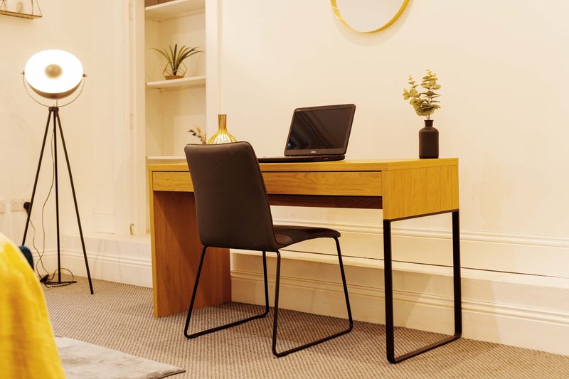 Modern home office with wooden desk, black chair, laptop, tripod lamp and gold accents