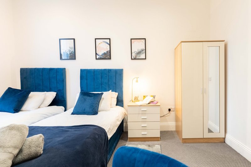 Bedroom with two single beds, blue headboards, white bedding, wooden wardrobe and nightstand