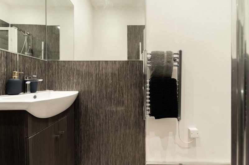 Modern bathroom with dark tile walls, white sink, mirror and towel rack
