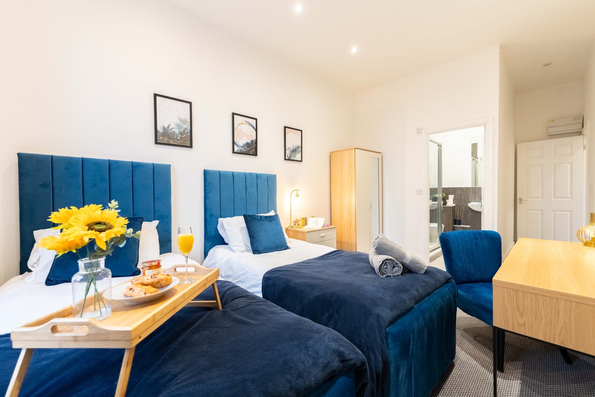 Twin bedroom with blue upholstered headboards, yellow flowers, wooden desk and ensuite bathroom