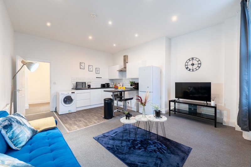 Open-plan living space with blue sofa, kitchen area, washing machine, and TV mounted on wall