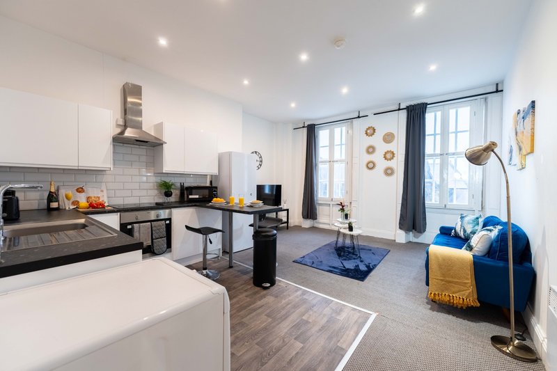 Open-plan studio apartment with kitchenette, work desk, and blue seating area