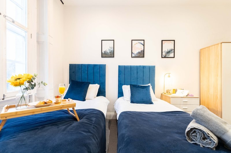 Bright twin bedroom with blue headboards, white pillows, dark bedding and wooden furniture