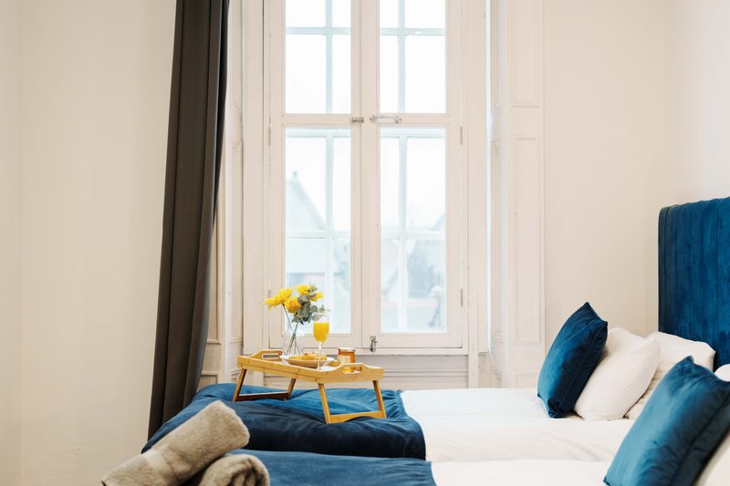 Bright bedroom with double bed, blue cushions, wooden tray table with flowers by window