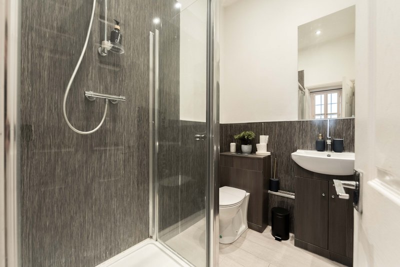Modern bathroom with walk-in shower, dark tile walls, white sink and toilet