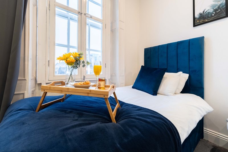 Bright bedroom with double bed, blue upholstered headboard, wooden breakfast tray and large window