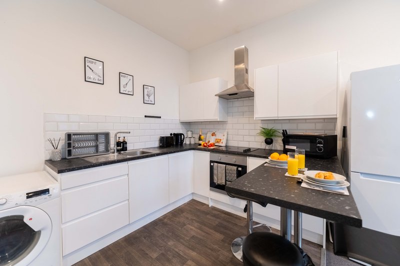Modern kitchen with white cabinetry, black countertops, stainless steel appliances and breakfast bar