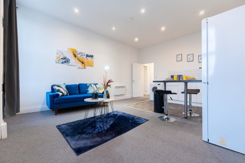 Open-plan living area with blue sofa, desk workspace, and modern white kitchen