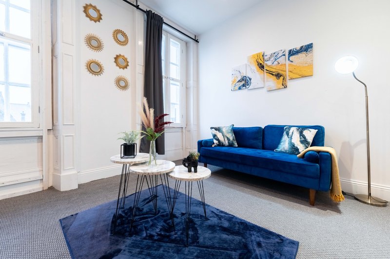 Bright living room with blue sofa, decorative wall art, side tables, and large windows