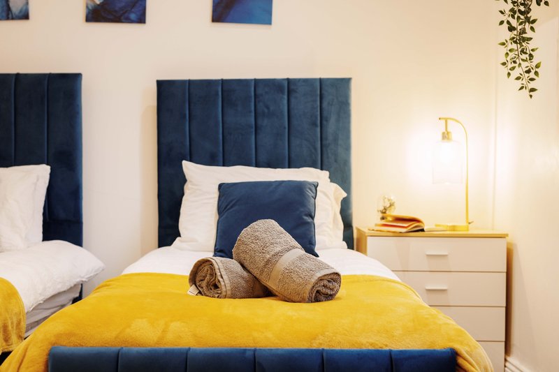 Modern bedroom with double bed, yellow bedding, blue headboard and bedside lamp