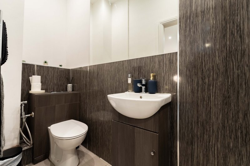 Modern bathroom with dark wood paneling, white sink, toilet, and toiletries