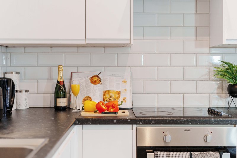 Modern kitchen with white subway tile backsplash, dark countertop, champagne bottle and fresh fruit
