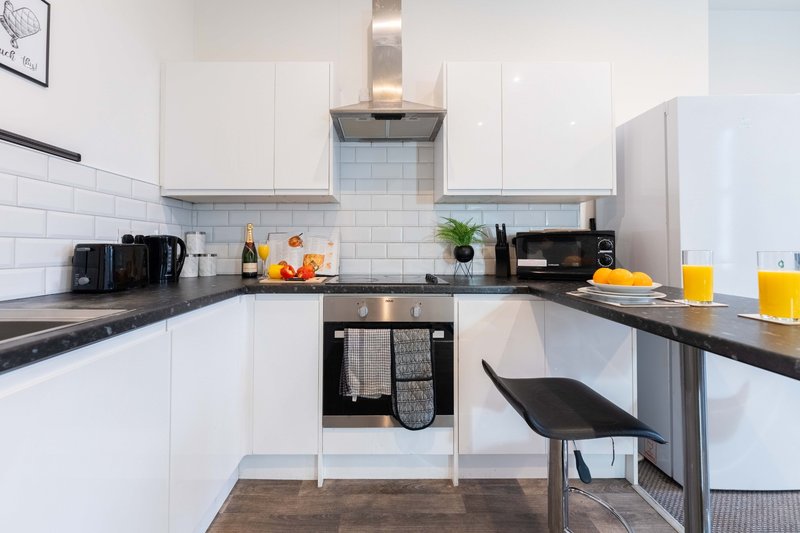 Modern white kitchen with black countertops, stainless steel hood, and breakfast bar seating