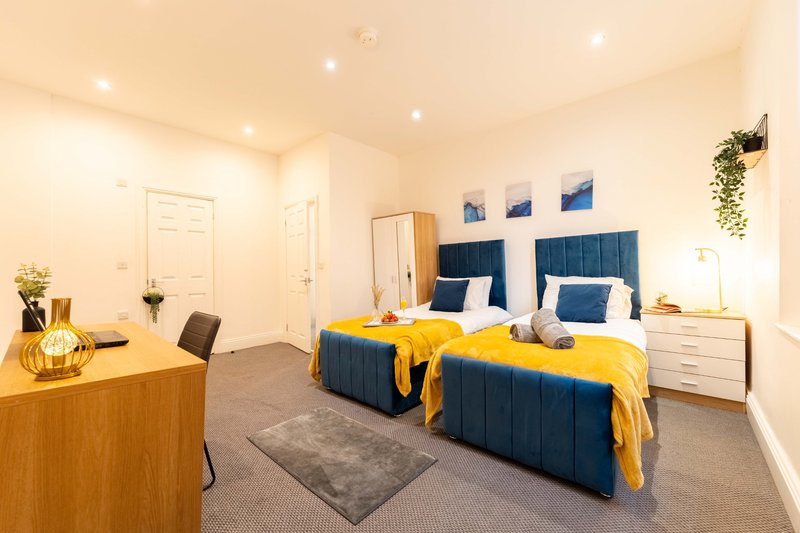 Modern bedroom with twin beds, blue headboards, yellow throws, wooden desk and pendant lighting