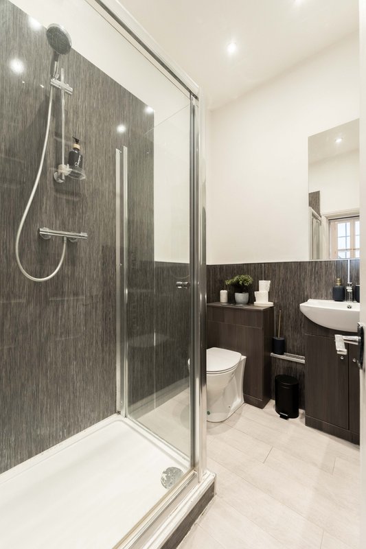 Modern bathroom with walk-in shower, dark tile walls, white sink and toilet