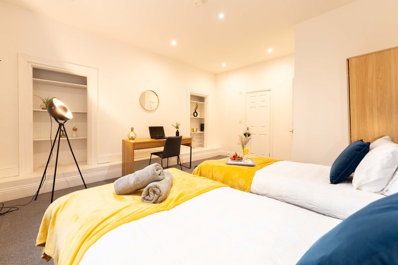 Modern bedroom with two beds, yellow bedding, desk area, and recessed ceiling lights