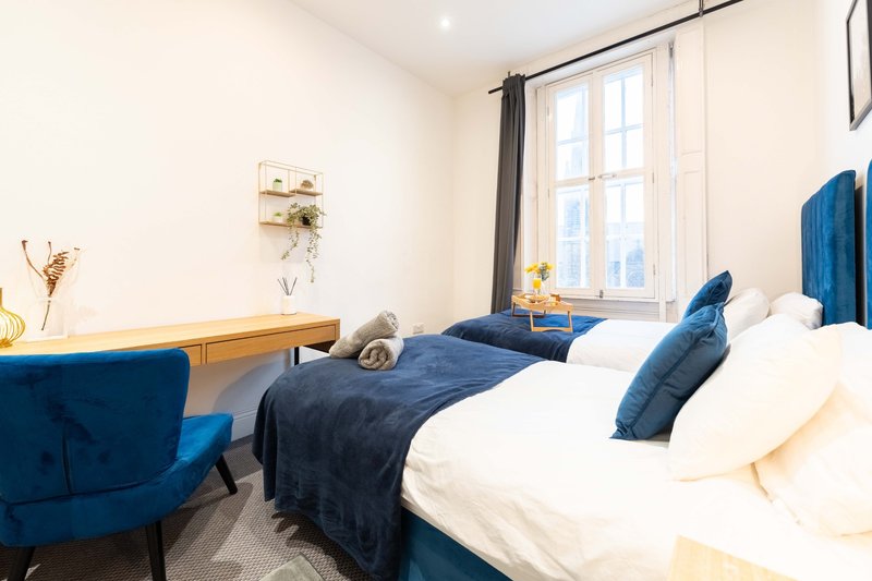 Bright bedroom with double bed, blue upholstered headboard, matching armchair, and large window