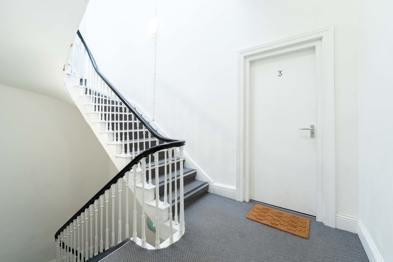 Modern spiral staircase with white railings, gray flooring and white door in bright hallway