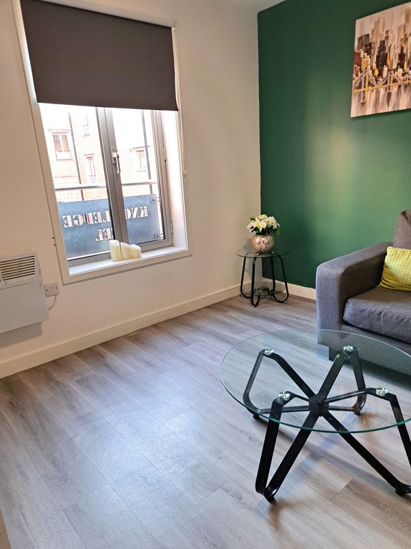 Modern living room with green accent wall, gray sofa, glass coffee table and large window