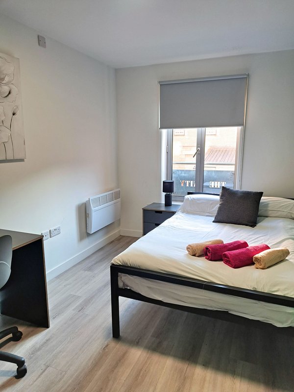 Bright bedroom with double bed, desk, chair, and glass door opening to balcony