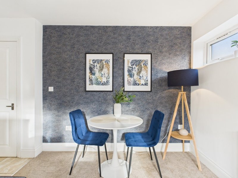 Modern dining area with round white table, two blue velvet chairs, and framed botanical artwork