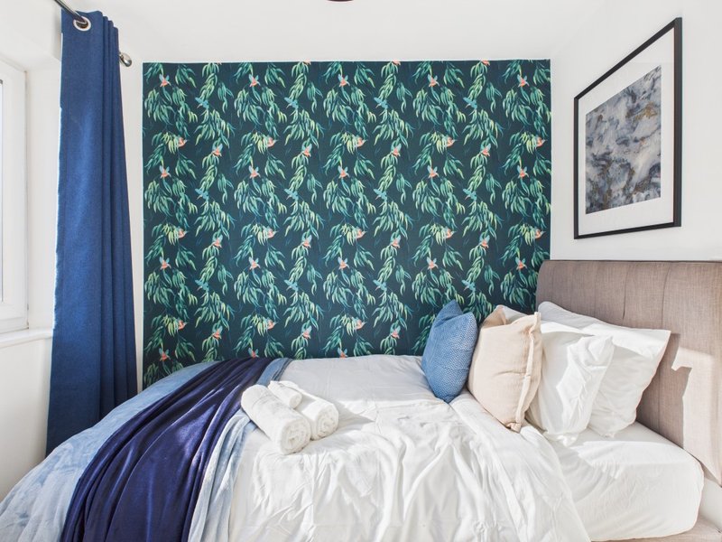 Modern bedroom with double bed, patterned green headboard wall, blue curtain and framed artwork