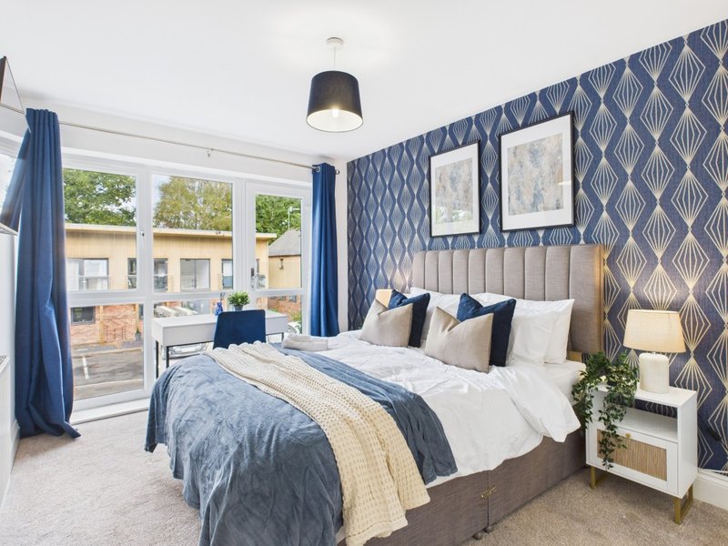Modern bedroom with double bed, blue patterned wallpaper, and patio doors overlooking garden