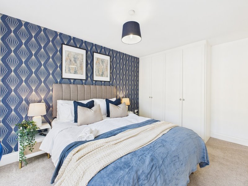 Modern bedroom with double bed, blue patterned accent wall, white wardrobe and pendant light